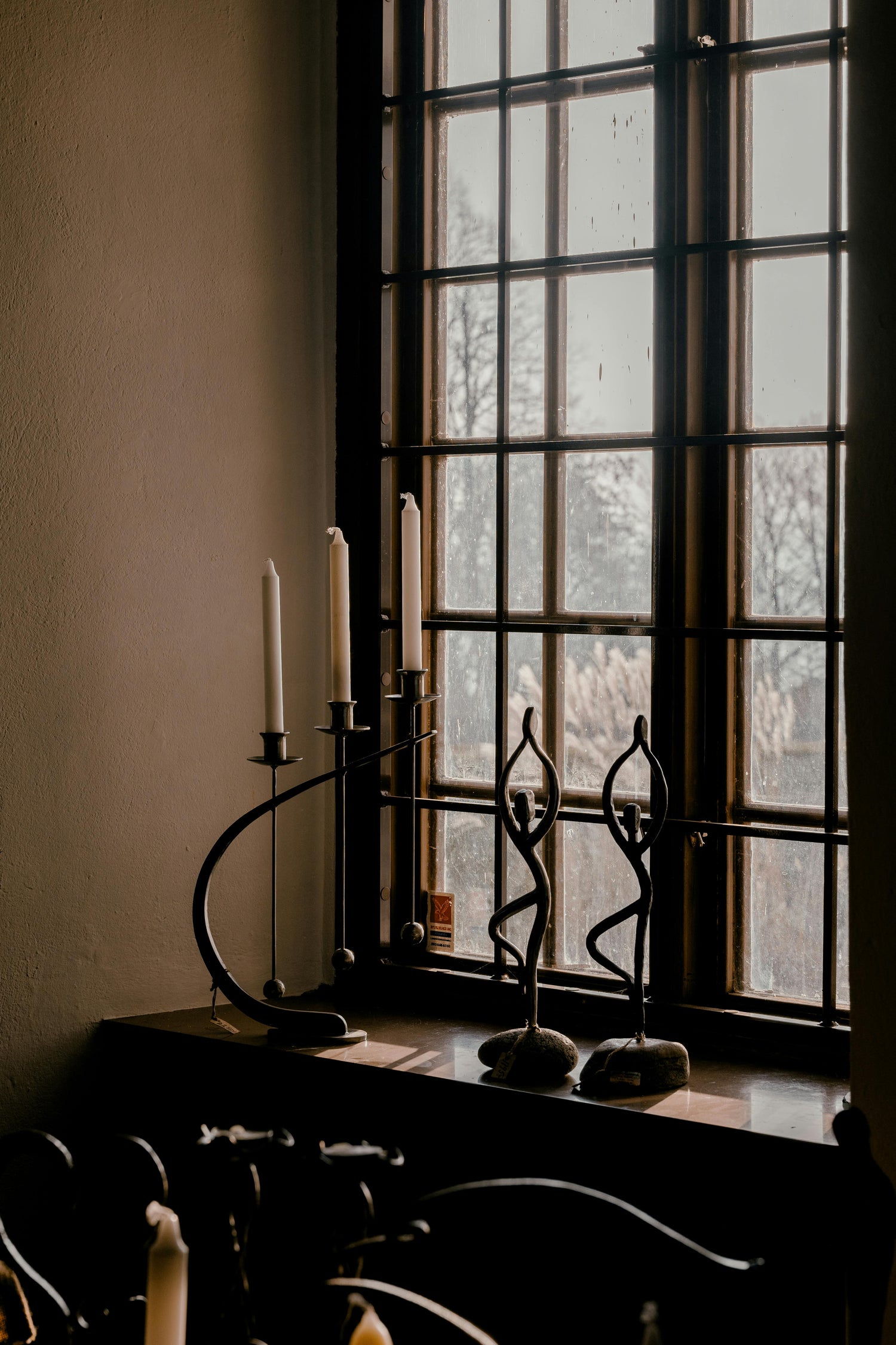 Sculptural black metal candlesticks arranged near a window with soft natural light.