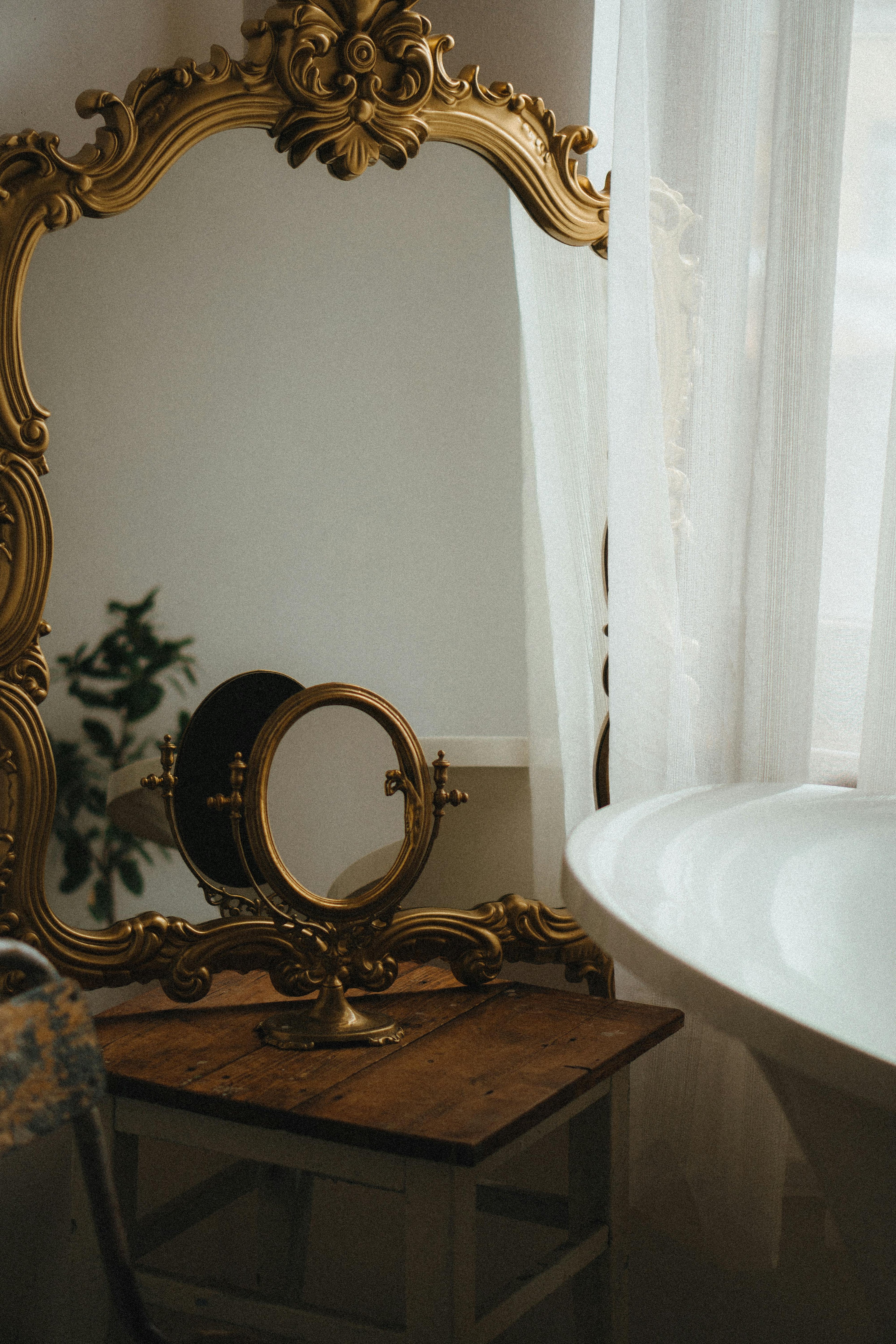 Moody vignette featuring a vintage gold mirror, soft drapery, and warm atmospheric lighting.